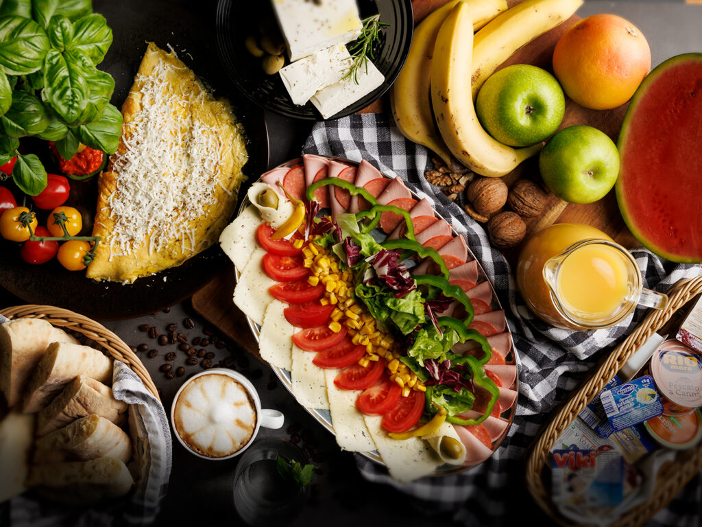 Kava ali čaj, juice, zelenjavno-mesni narezek, omleta, lepinja, namazi (maslo, med, čokoladni namaz, pašteta), jogurt, sadje…